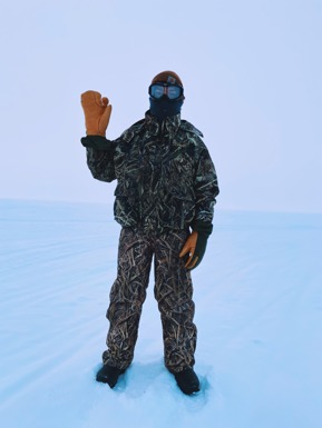 Man with heavy clothing and goggles waves on the tundra.