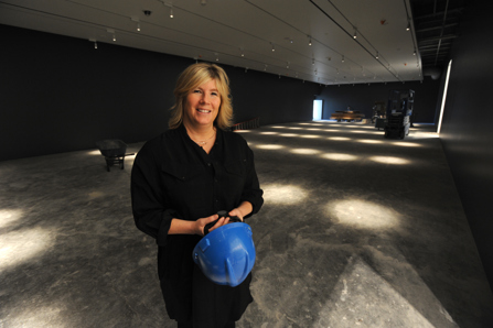 Woman standing near a construction scene, holding a blue hard hat and smiling