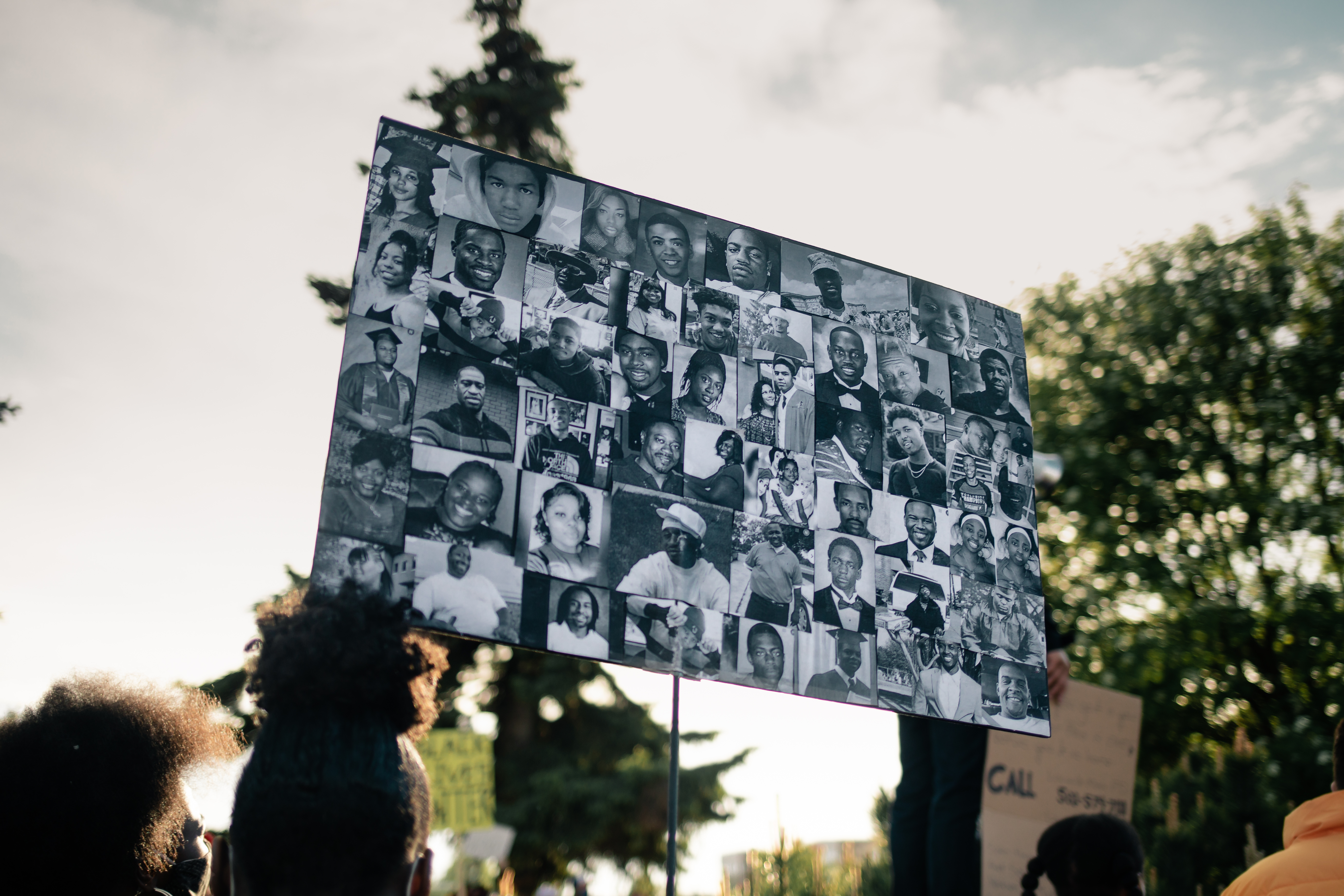 Protester holding a poster representing Black people killed by police (Breonna Taylor, second-to-last row, third from left), 2020